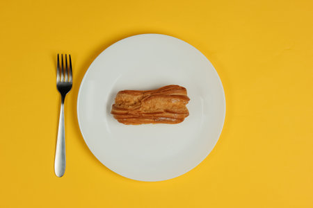 Eclair in plate with fork on yellow background. Top viewの写真素材