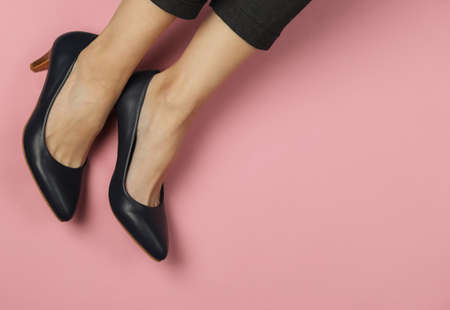 Female legs dressed in trousers and classic shoes with heels on pink pastel background. Top view....