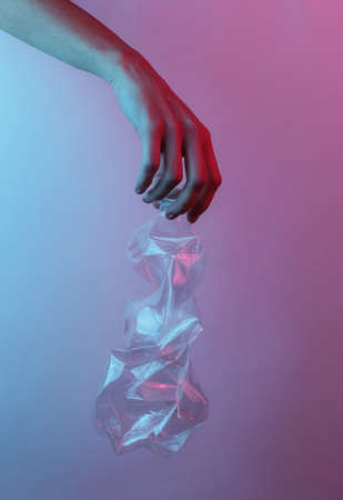 Recycling concept. Female hand holds a rumpled plastic bottle. Creative pop art pink blue neon...