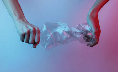 Recycling concept. Female hand holds a rumpled plastic bottle. Creative pop art pink blue neon...