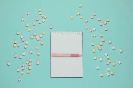 Notebook with pen and lot of marshmallows on blue pastel background. Top view