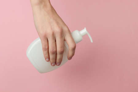 Minimalism beauty concept. Female hand hold a bottle of cream on pink pastel background. Studio shot