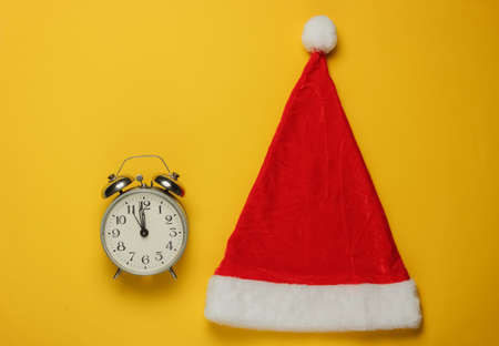 Santa hat and alarm clock on yellow background. New Year, Christmas minimalistic concept. Top view, studio shot.の写真素材