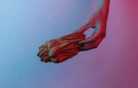 Female hand holds an eclair. Creative pop art pink blue neon color. Trendy gradient illumination. Night lightの写真素材