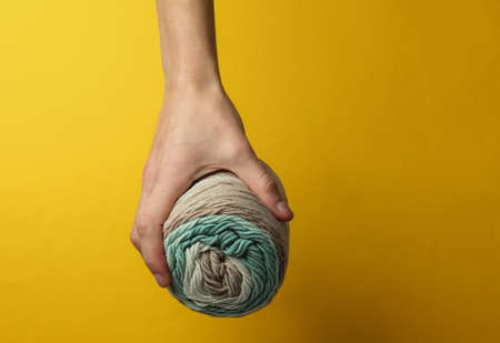 Female hand holds a skein of woolen threads on a yellow studio background.の写真素材