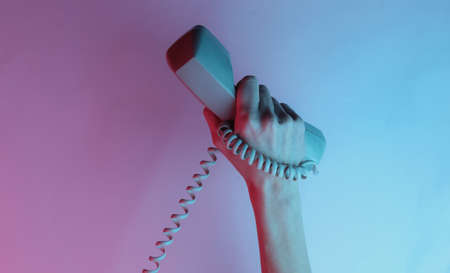 Female hand wrapped in cable holds retro handset. Creative pop art pink blue neon color. Trendy...