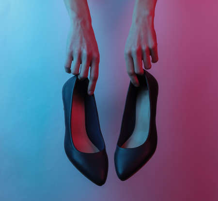 Women's hands hold classic high heel shoes. Creative pop art pink blue neon color. Trendy gradient...