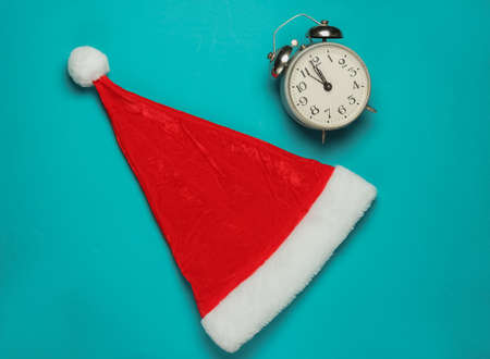 Santa hat and alarm clock on blue background. New Year, Christmas minimalistic concept. Top view,...