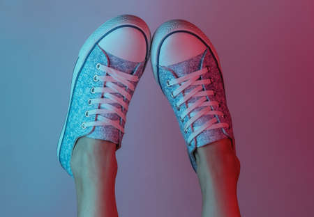 Women's feet with sneakers. Creative pop art pink blue neon color. Trendy gradient illumination. Night lightの写真素材