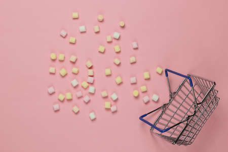 Lot of mini marshmallows and shopping basket on pink background. Pastel color trend. Top view