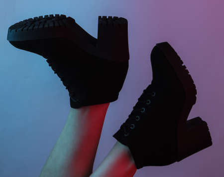 Women's feet with black boots. Creative pop art pink blue neon color. Trendy gradient illumination. Night lightの写真素材