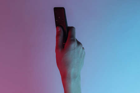 Female hand holds tv remote. Creative pop art pink blue neon color. Trendy gradient illumination. Night lightの写真素材