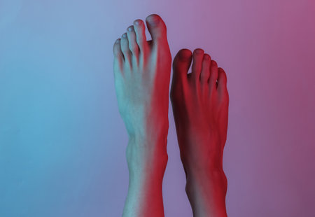 Barefooted female legs close-up. Creative pop art pink blue neon color. Trendy gradient illumination. Night lightの写真素材