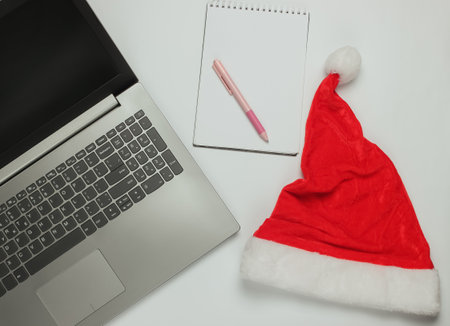 Laptop with santa hat, notebook on white background. Letter to santa, wish list.の写真素材