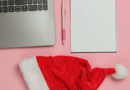 Laptop with santa hat, notebook on pink pastel background. Letter to santa, wish list.の写真素材