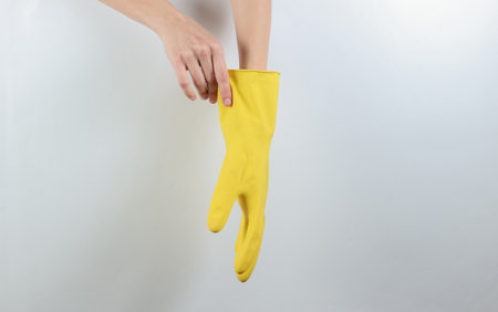 House cleaning concept. Female hands wear yellow rubber gloves for cleaning on a gray background