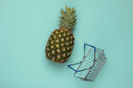 Shopping basket and pineapple on a blue pastel background. Top viewの写真素材