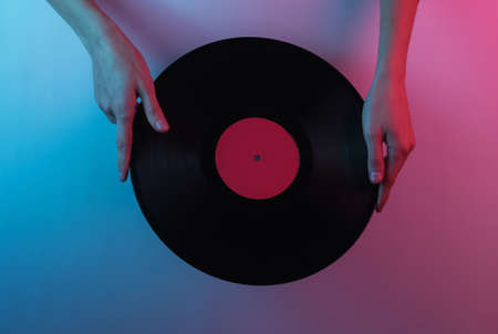 Retro wave 80s. Hands holding vinyl record. Creative pop art pink blue neon color. Trendy gradient illumination. Night lightの写真素材