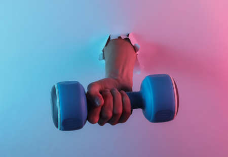 Hand holds dumbbell through torn hole. Creative pop art pink blue neon color. Trendy gradient illumination. Night lightの写真素材