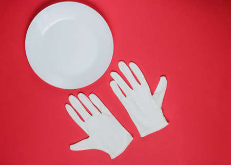 White waiter gloves and empty ceramic plate on a red studio background. Top viewの写真素材