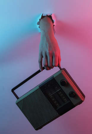 Female hand holds a radio receiver through torn hole. Creative pop art pink blue neon color. Trendy gradient illumination. Night lightの写真素材