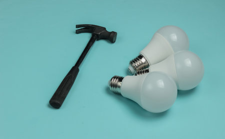 Three LED light bulbs and a hammer on a blue background.