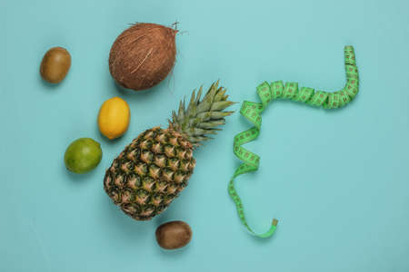The concept of losing weight. Tropical fruits and measuring tape on a blue background. Healthy...