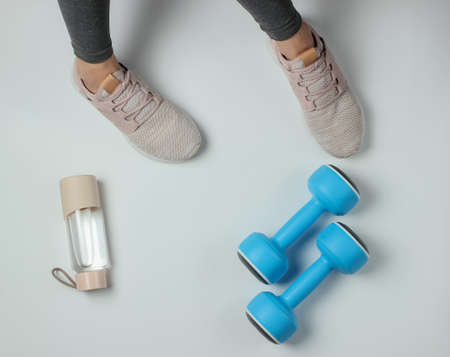 Fitness, sport concept. Female legs dressed in leggings and sneakers are sitting on a white...