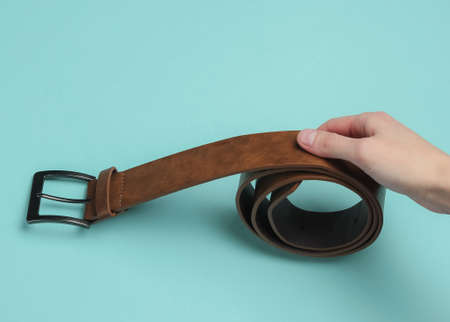Female hand holds a leather brown belt on blue backgroundの写真素材