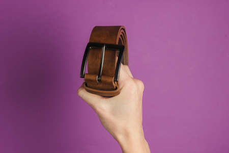 Female hand holds a leather brown belt on purple backgroundの写真素材
