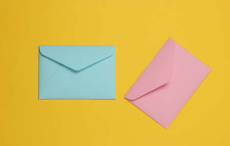 Two envelopes of pink and blue pastel colors on a yellow background. Flat lay mockup for valentines...