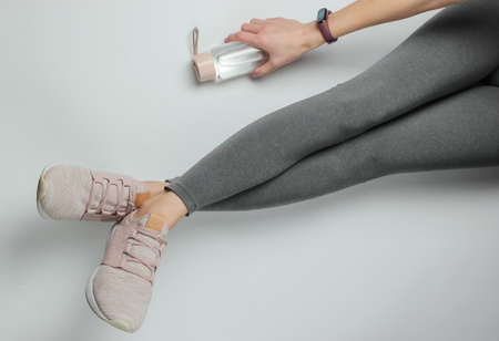 Fitness, sport concept. Female legs dressed in leggings and sneakers are sitting on white background with a bottle of water for training. Top viewの写真素材