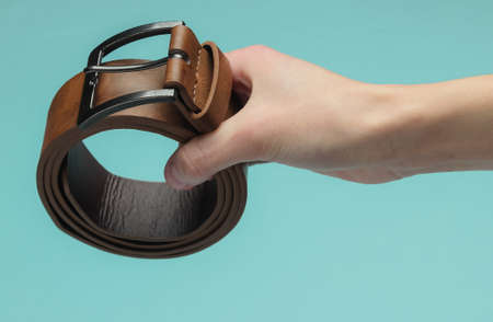 Female hand holds a leather brown belt on blue background