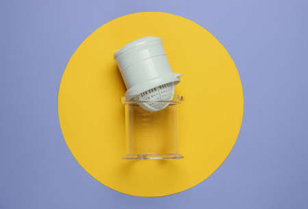 Plastic manual juicer on purple background with yellow circle. Top view