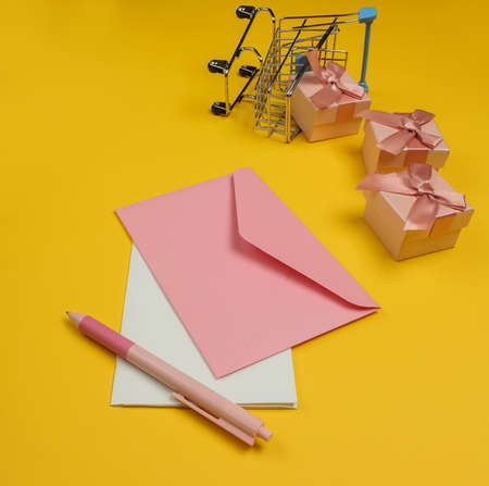 Envelope with letter and pen, boxes of gifts, shopping trolley on yellow background. Christmas, Valentine's day, birthday.の写真素材