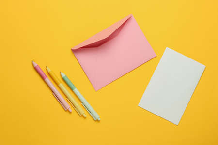 Envelope with a letter and pens on yellow background. Valentine's day, wedding or birthday. Top viewの写真素材