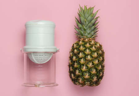 Plastic manual juicer and pineapple on pink pastel background. The concept of healthy nutrition,...