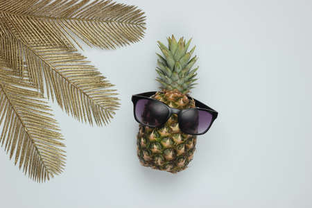 Pineapple with sunglasses and golden palm leaves on white background. Tropical concept. Top viewの写真素材