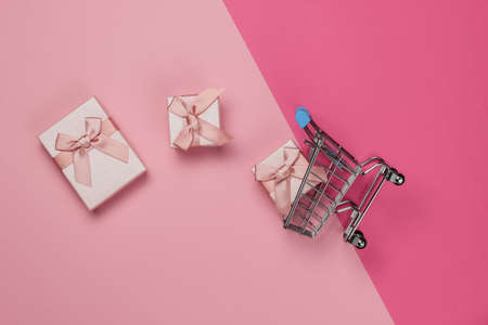 Shopping trolley and gift boxes with bows on pink pastel background. Composition for christmas, birthday or wedding.の写真素材