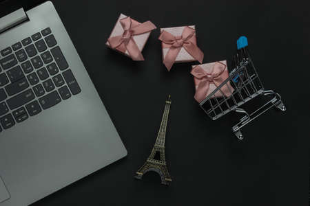 Online shopping. Laptop and gift boxes with bows, eiffel tower figurine on black background. Top...