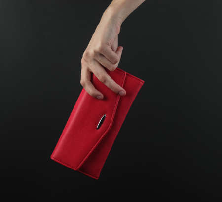 Female hand holds a red leather purse on a black backgroundの写真素材
