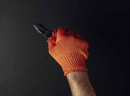 Hands with work gloves are holding pliers on black background. Industrial worker