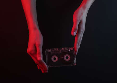 Female hands holding a retro audio cassette on black background with red neon lightの写真素材