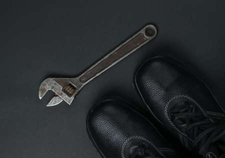 Work leather shoes and wrench. Industrial working tools and instruments, safety equipmen on black...