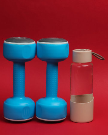 Accessories for fitness and sports on red background. Dumbbells, bottle of water.