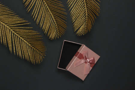 Open Gift box on a black background with golden palm leaves. Fashion flat lay. Top view