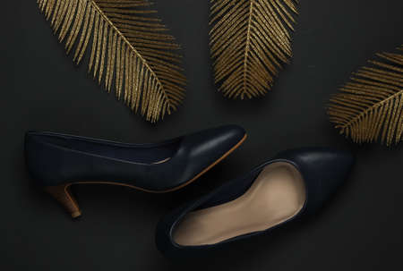 Women's classic leather high heel shoes on a black background with gold palm leaves. Rich concept. Fashion flat lay. Top viewの写真素材