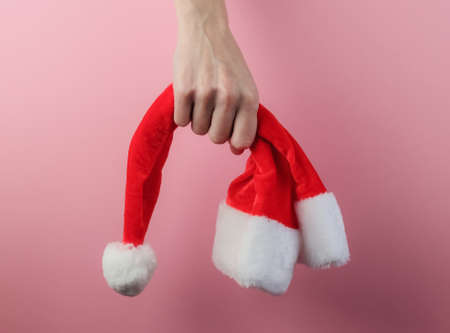 Christmas concept. Female hands hold santa hat on pink pastel backgroundの写真素材