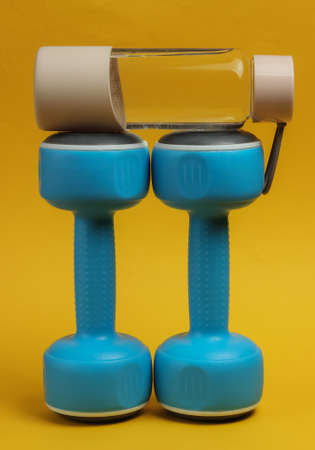 Accessories for fitness and sports on yellow background. Dumbbells, bottle of water.の写真素材