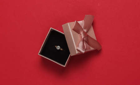 Gift box and engagement gold ring with diamond on a red background. Wedding, romantic concept....